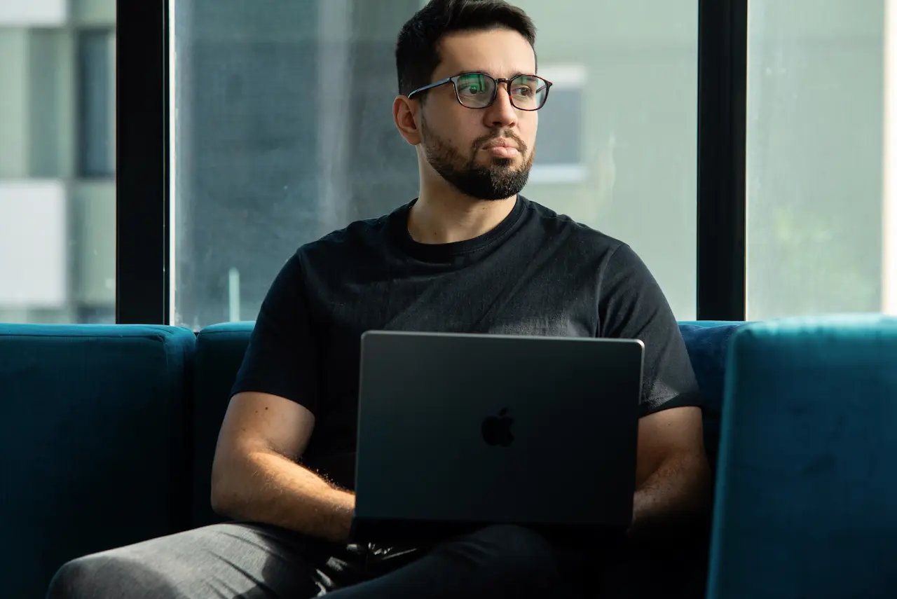 Rafael Machado sentado em um sofá, no escritório, olhando para o lado ao posar para uma foto com seu computador.